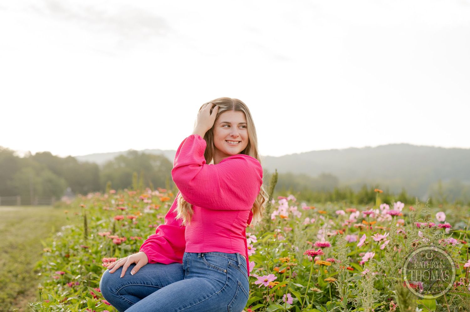 Joyful outdoor photo in a vibrant pink sweater surrounded by wildflowers and rolling hills.