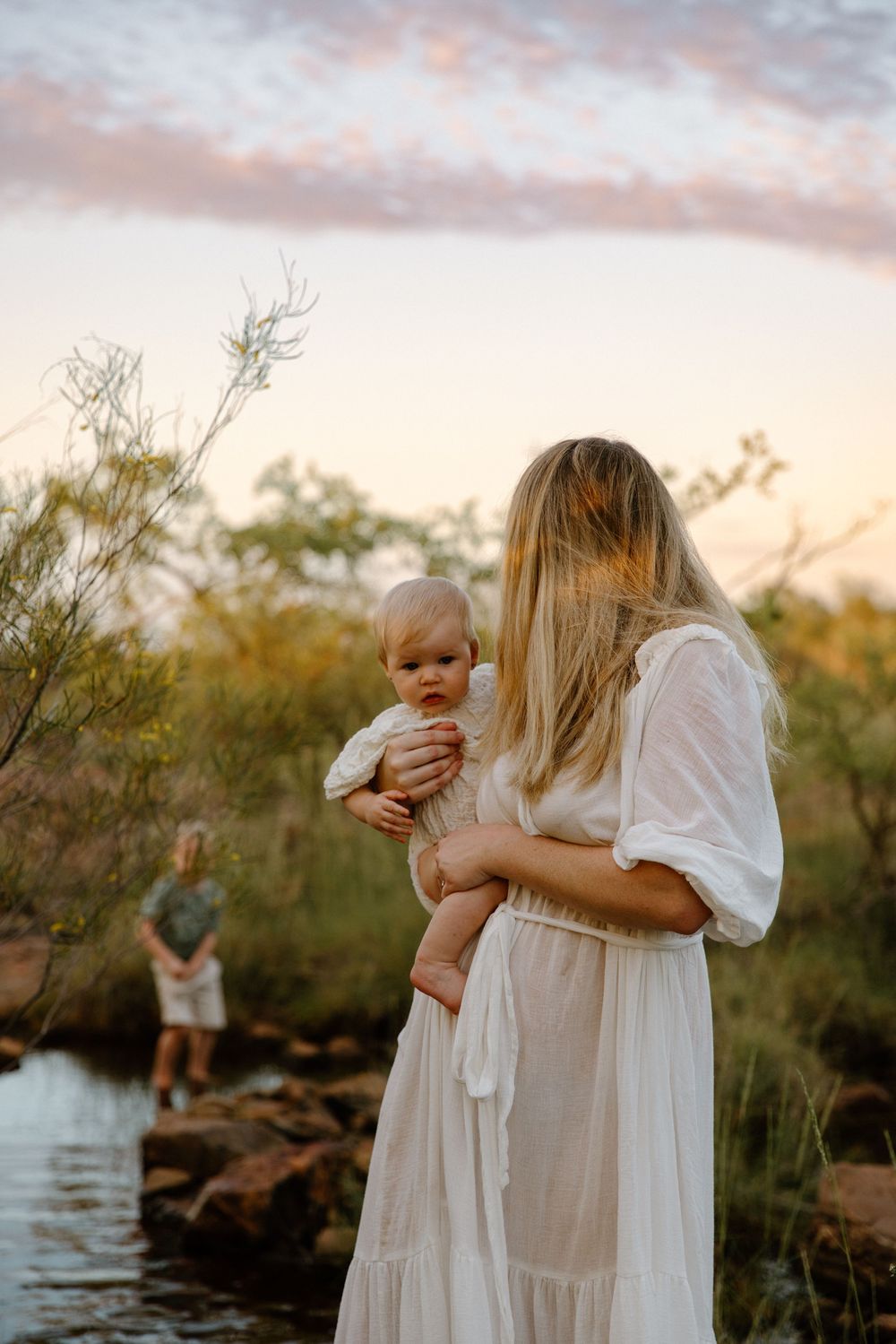 A tranquil sunset scene with light flowing white dresses against a backdrop of trees and water.