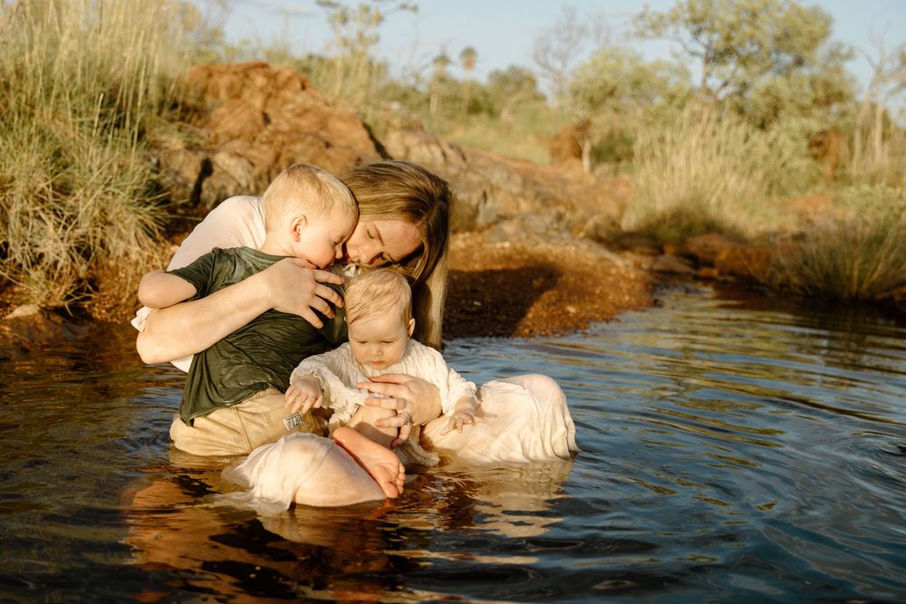 Tender family moment captured in a natural swimming hole surrounded by golden grass in the late afternoon sun.
