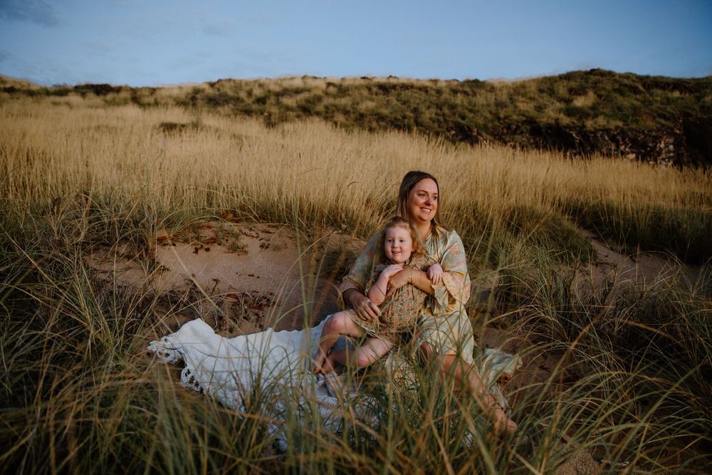 A sunset portrait in tall coastal grass with a white dress contrasting against the warm evening light and natural scenery.