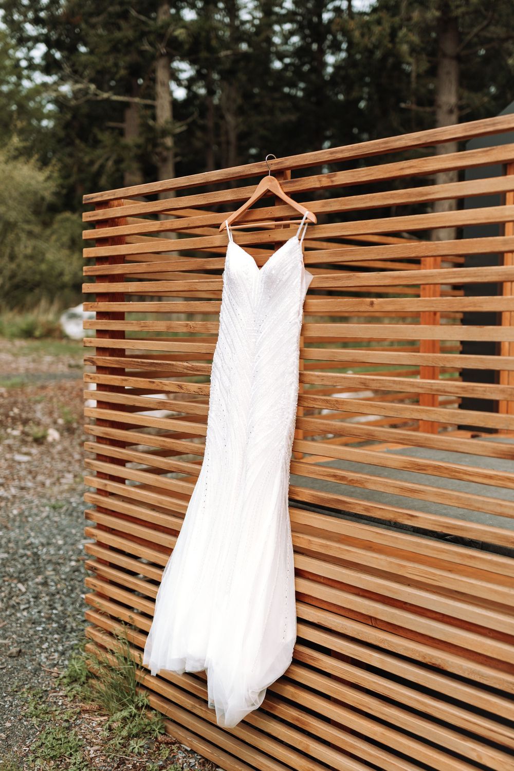 White wedding dress hanging on wooden slatted wall backdrop in outdoor setting.
