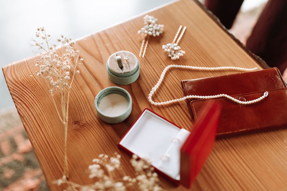 Wedding details including delicate baby's breath flowers, rings, and a red velvet pouch on a wooden surface.