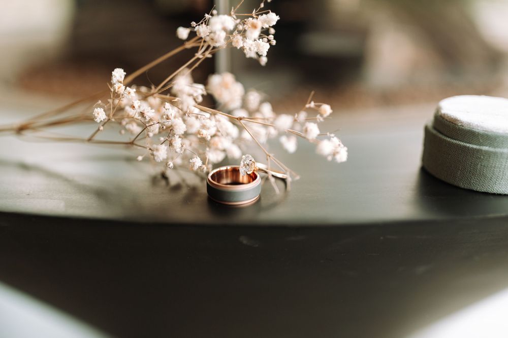 Wedding rings and baby's breath flowers arranged on a dark surface in soft focus.