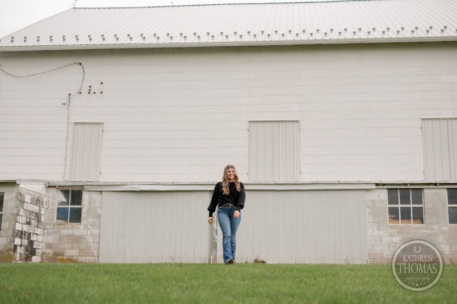 Wide shot of person in casual attire standing against large white barn building.