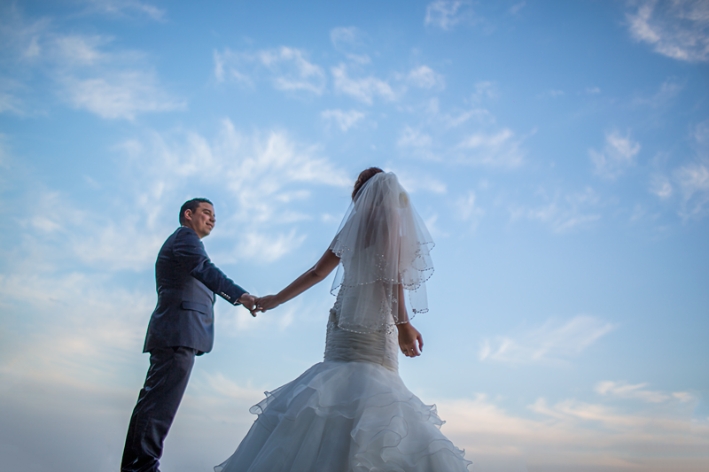 A couple shares a romantic moment against a blue sky on their wedding day.