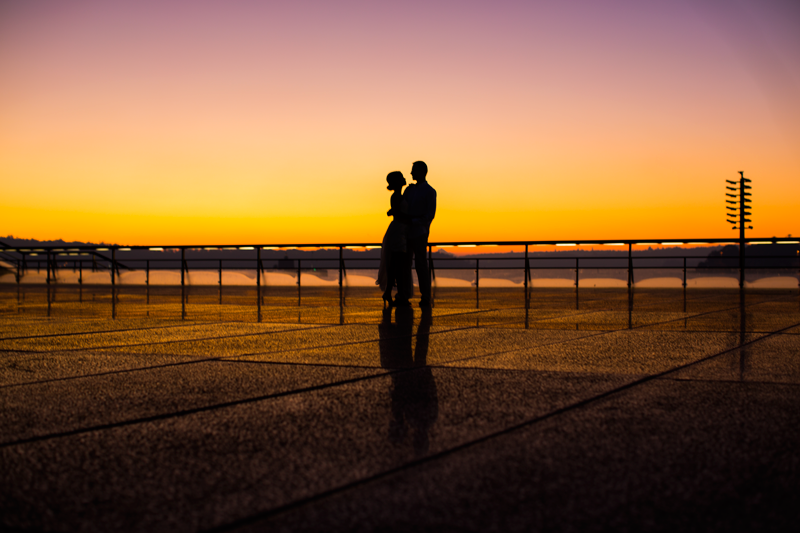 Silhouette of a couple standing together against a dramatic orange sunset sky.