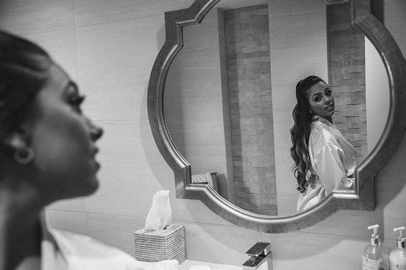 A black and white reflection in an ornate mirror shows preparation moments before a wedding.