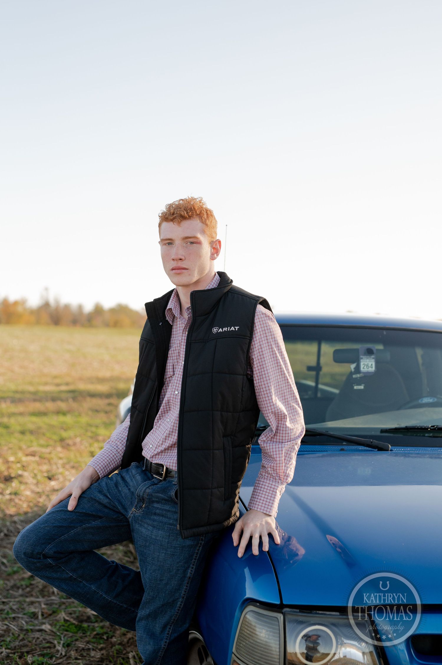 A portrait showcasing someone standing next to a blue truck in an open field.