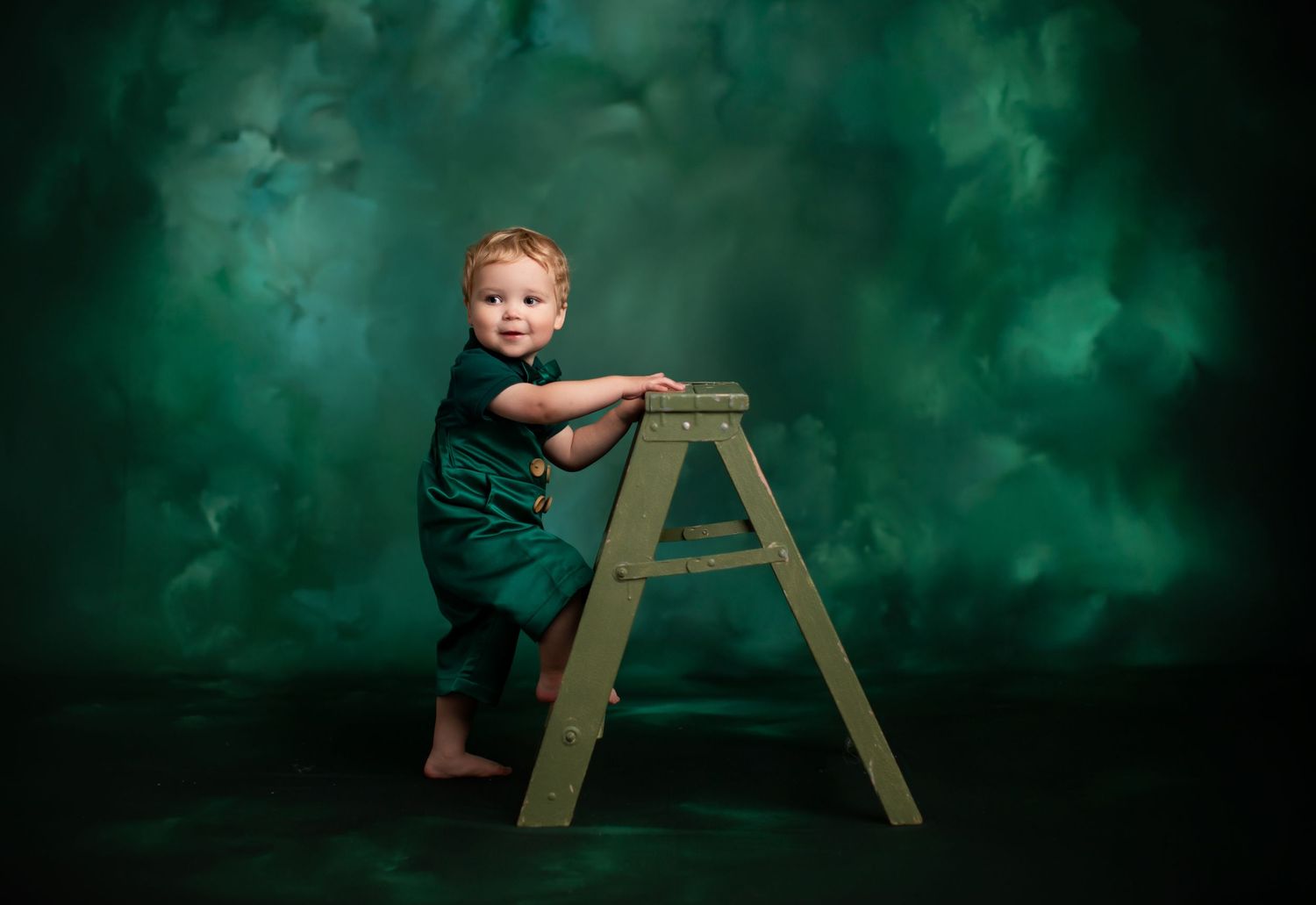 A small child stands on a wooden stepladder against a dramatic green smoky background.
