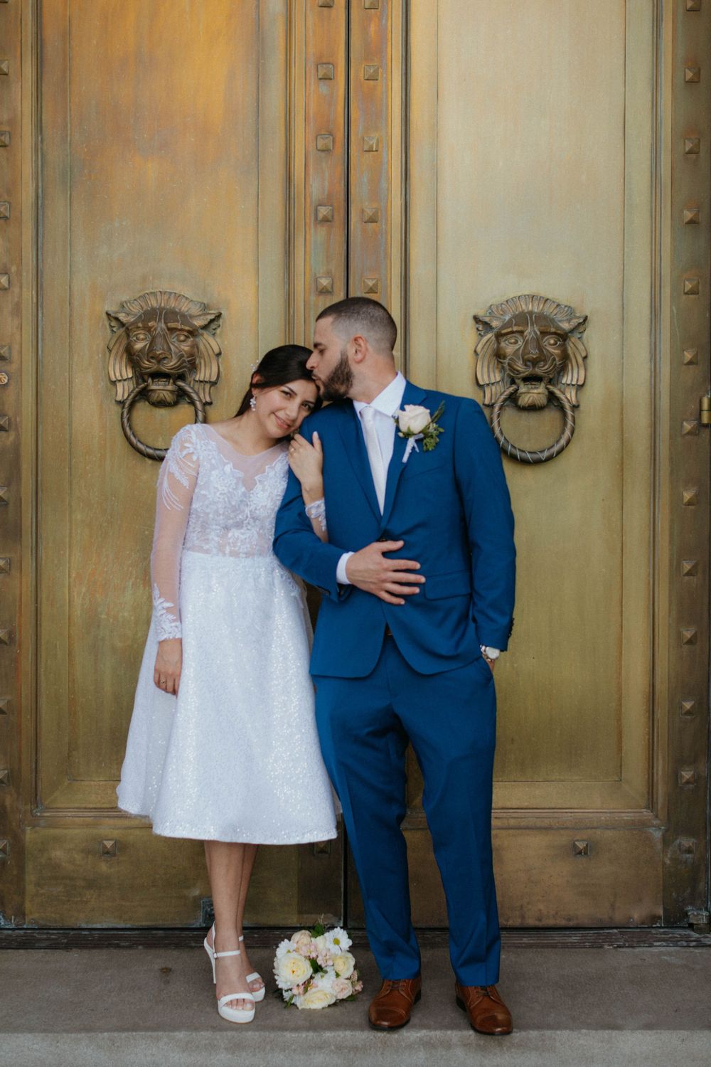 A wedding couple standing against a gold door, the bride in white lace and groom in navy blue suit. Denver Colorado elopement