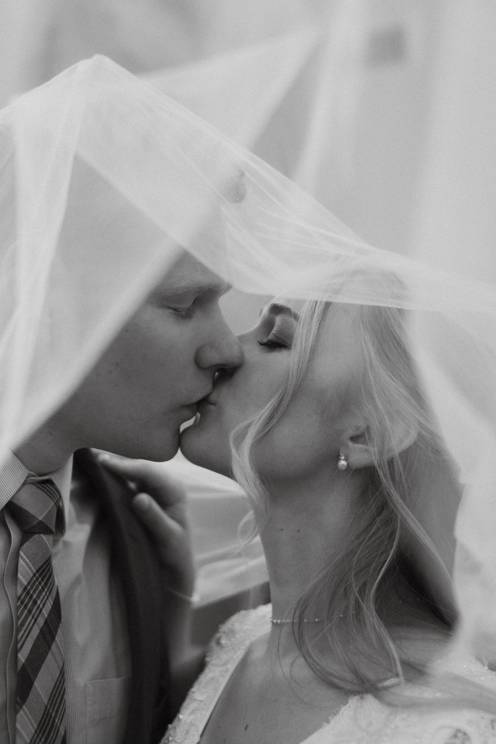 A romantic black and white wedding photograph showing a tender kiss under a delicate veil. Colorado timeless wedding