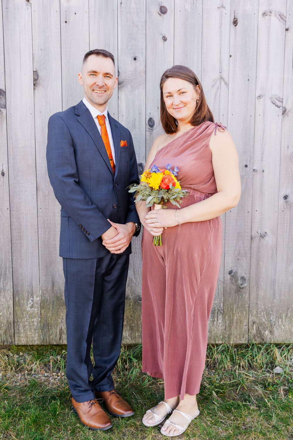 Groomsman in navy suit and bridesmaid in dusty rose dress pose with fall bouquet.