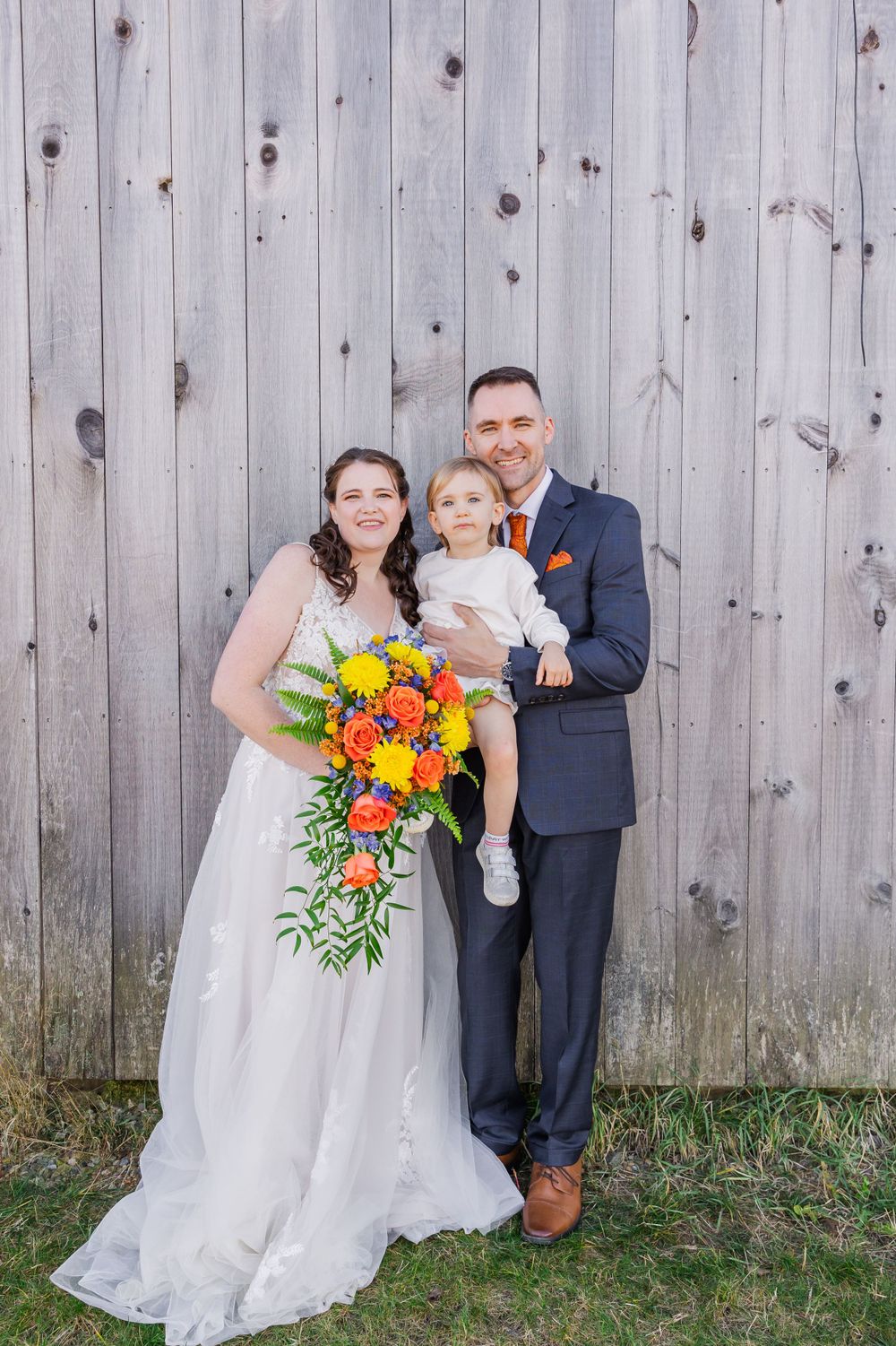 Elegant wedding portrait against rustic wooden backdrop with vibrant cascading floral bouquet.