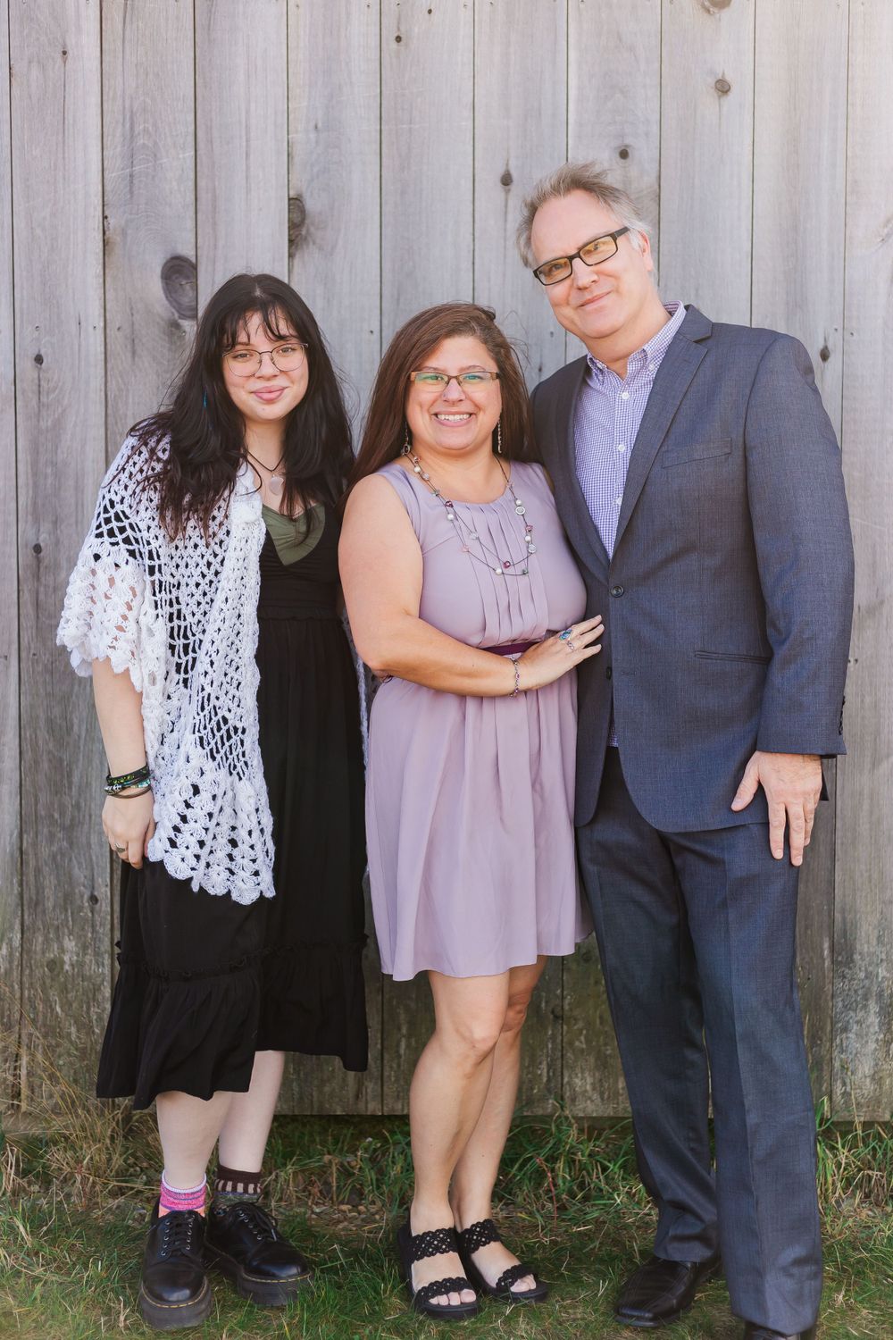 Family of three poses against weathered wooden wall wearing coordinated blue and purple outfits.