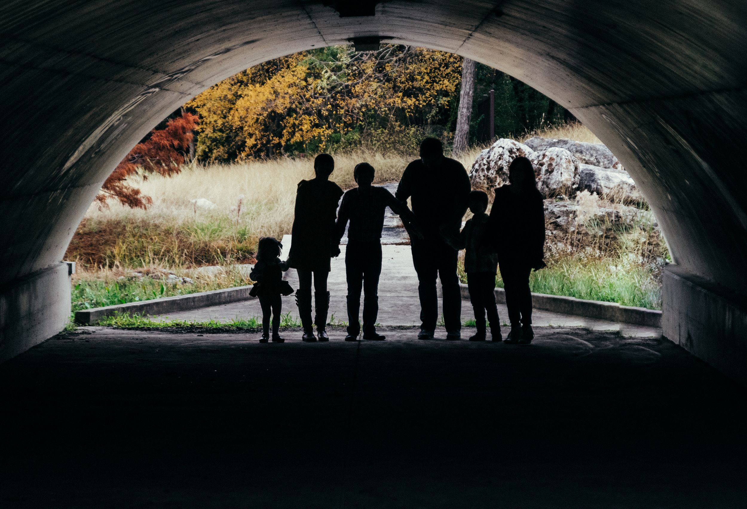 Silhouetted family standing in a tunnel entrance with autumn foliage visible in the background.