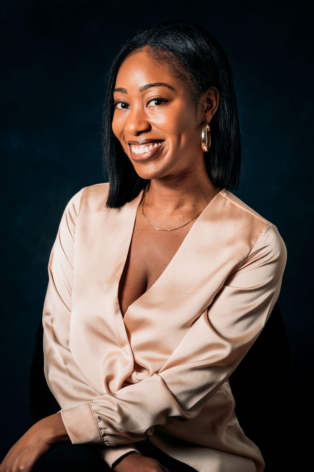 Professional portrait against dark background featuring person in elegant champagne-colored blazer.