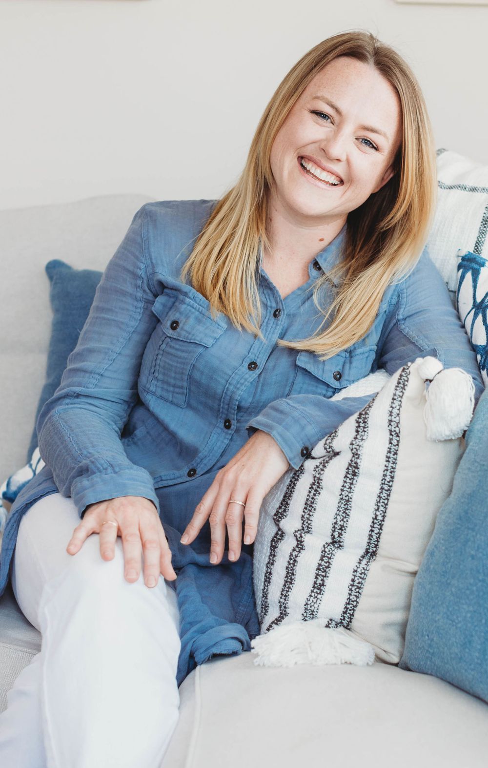 Casual portrait of person in denim shirt sitting on white couch with striped pillows.