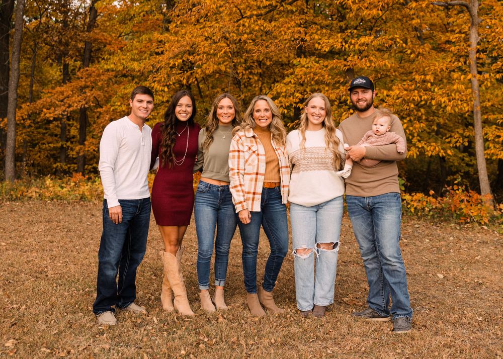 Family of seven, including a baby, poses together in autumn fall foliage with bright orange leaves in a wooded outdoor setting.