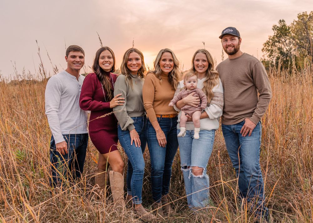 Family of seven with a baby poses in a golden grass field at sunset for an autumn family portrait.