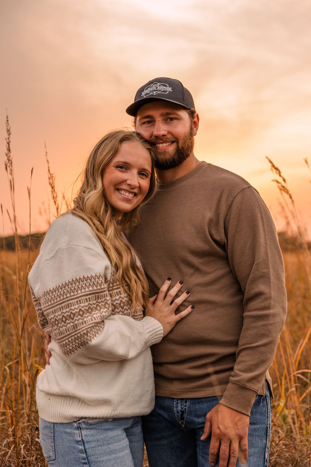 A happy couple in a warm embrace outdoors at sunset, the man in a baseball cap and the woman in a knit sweater.
