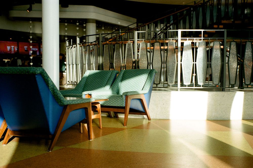 Modern lounge area with blue and green chairs in sunlit interior space.