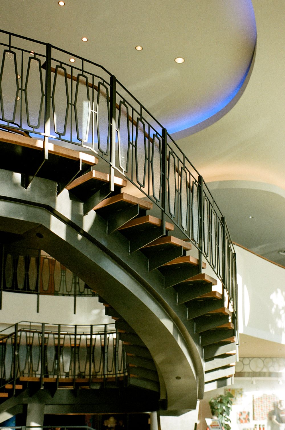 Modern curved staircase with wooden steps and metal railings under ambient lighting.
