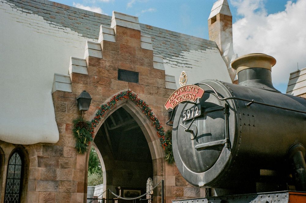 A vintage-style train engine display with stone archway entrance at a theme park.