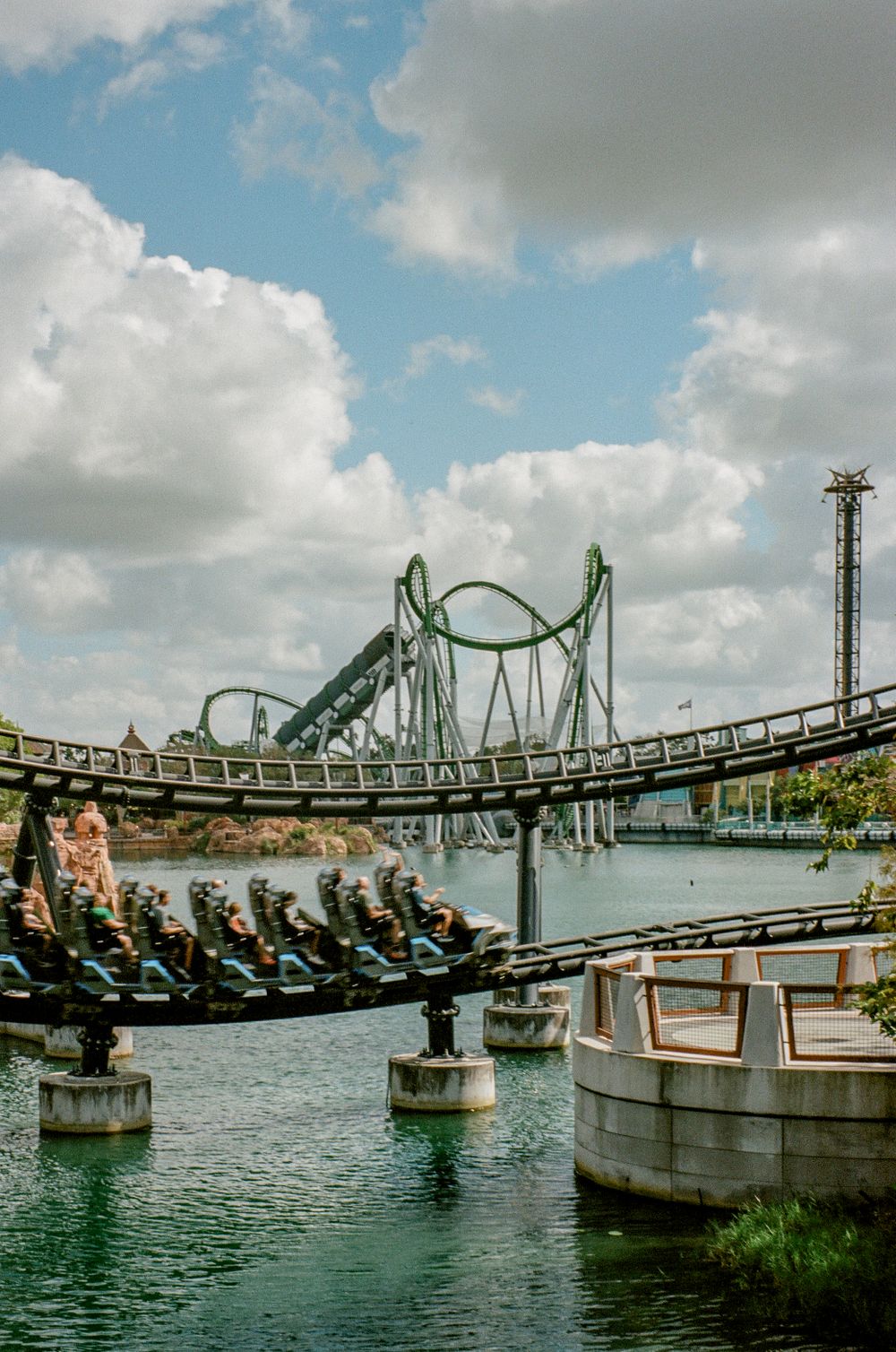 A roller coaster track spans across water with dramatic loops and turns against a cloudy sky.