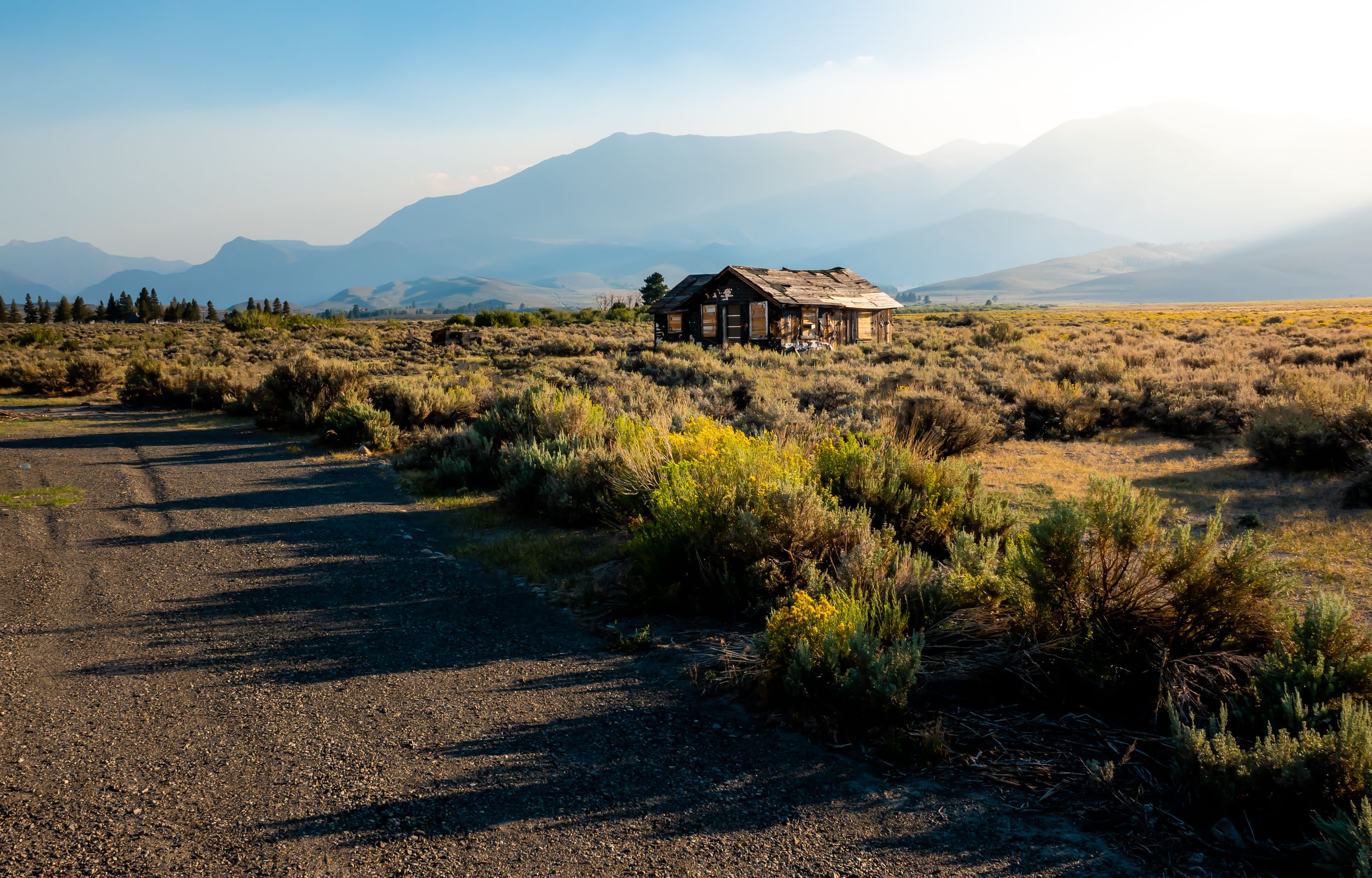 Rustic cabin stands alone in a desert landscape with mountain backdrop at golden hour.