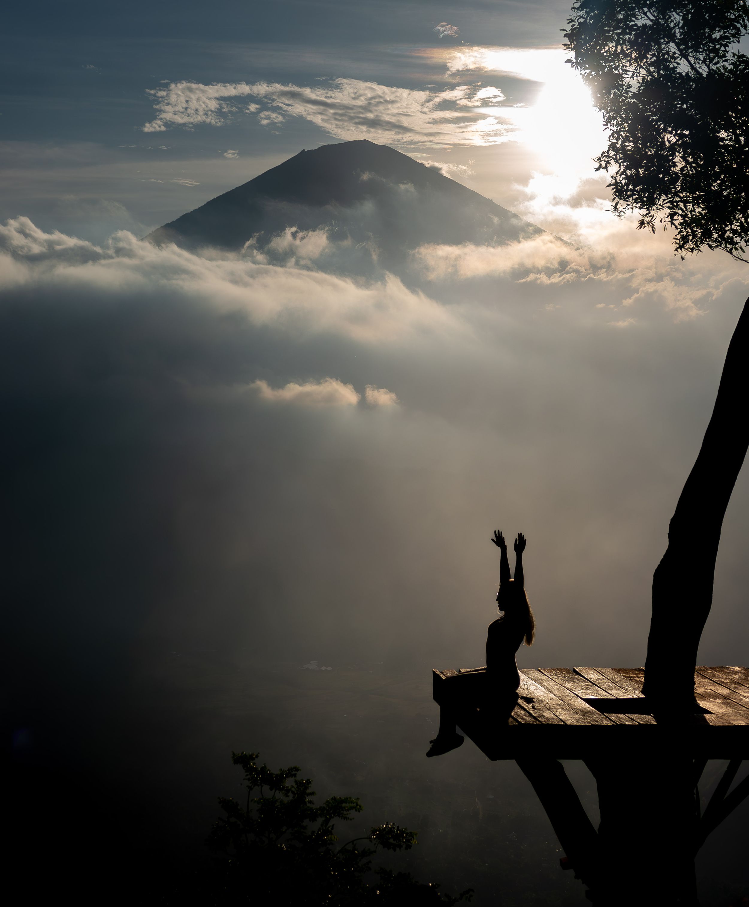 Silhouette of mountain peak with dramatic clouds and figure sitting on wooden platform.