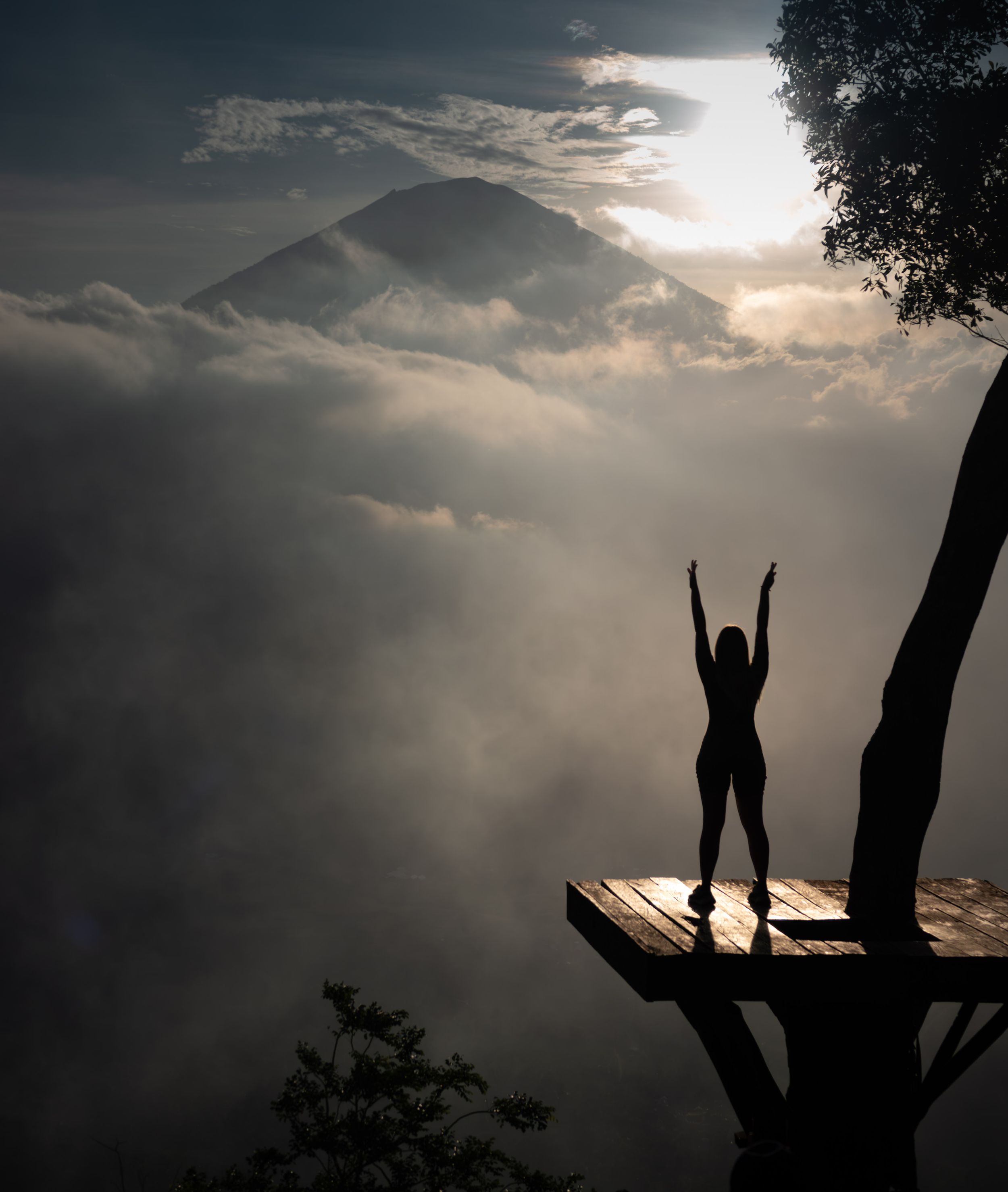 Silhouette of a figure celebrating at sunrise on a mountain viewpoint above misty clouds.