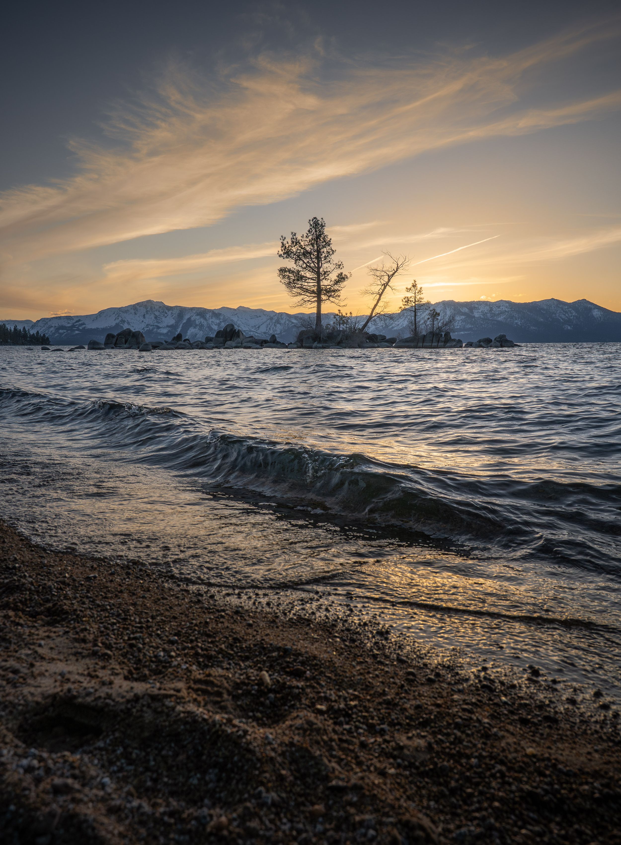 Dramatic sunset over Lake Tahoe with rolling waves and snow-capped mountains in the distance.