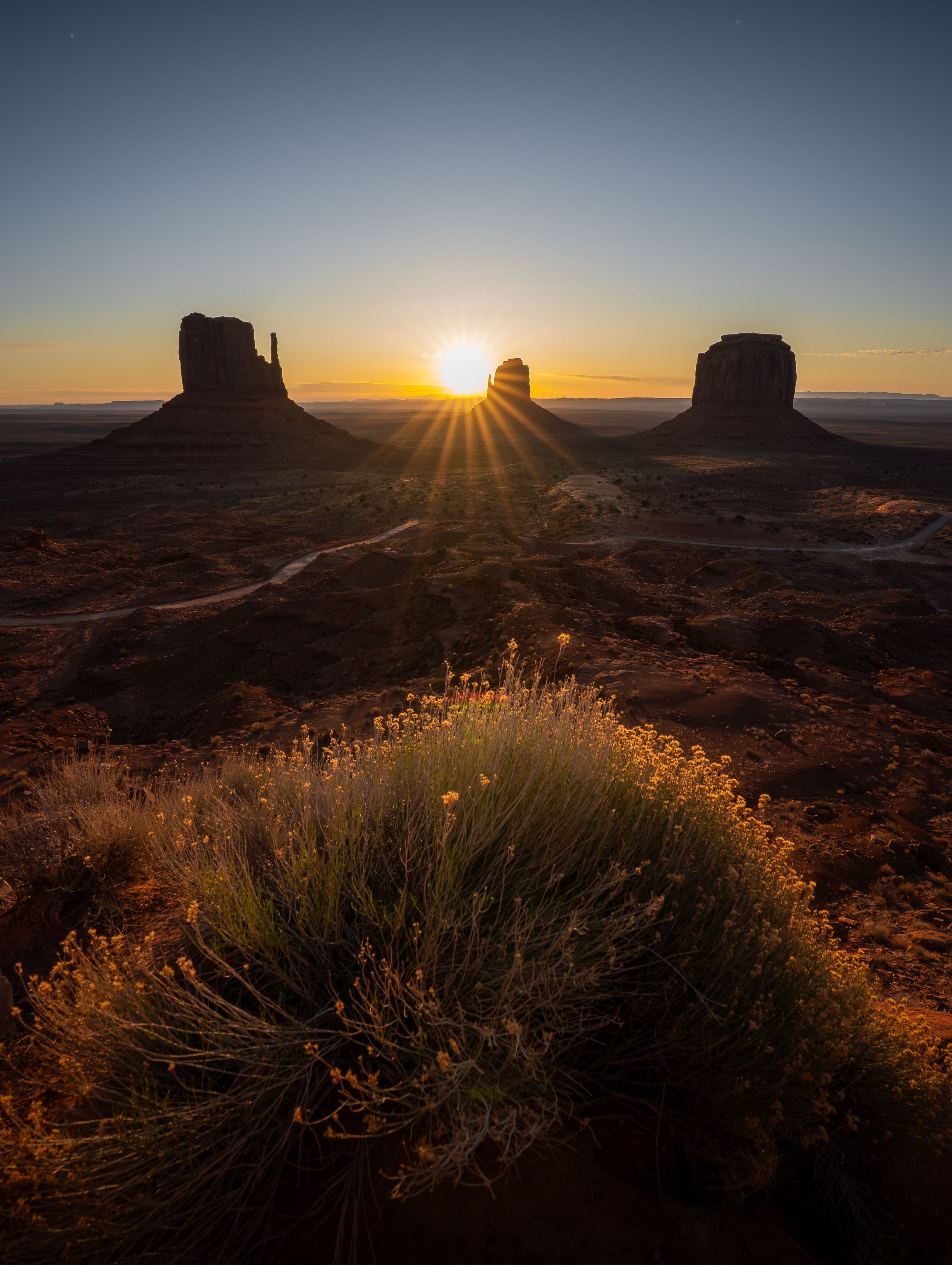 Dramatic sunrise silhouettes the iconic rock formations of Monument Valley against a golden desert sky.
