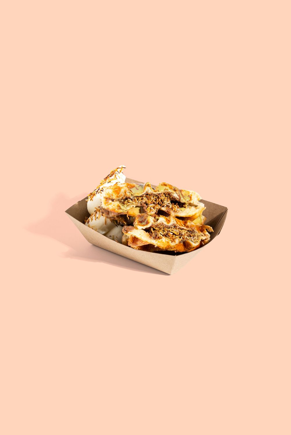 Loaded sandwich with toppings served in a disposable paper tray on peach background. Mtlshutter photography