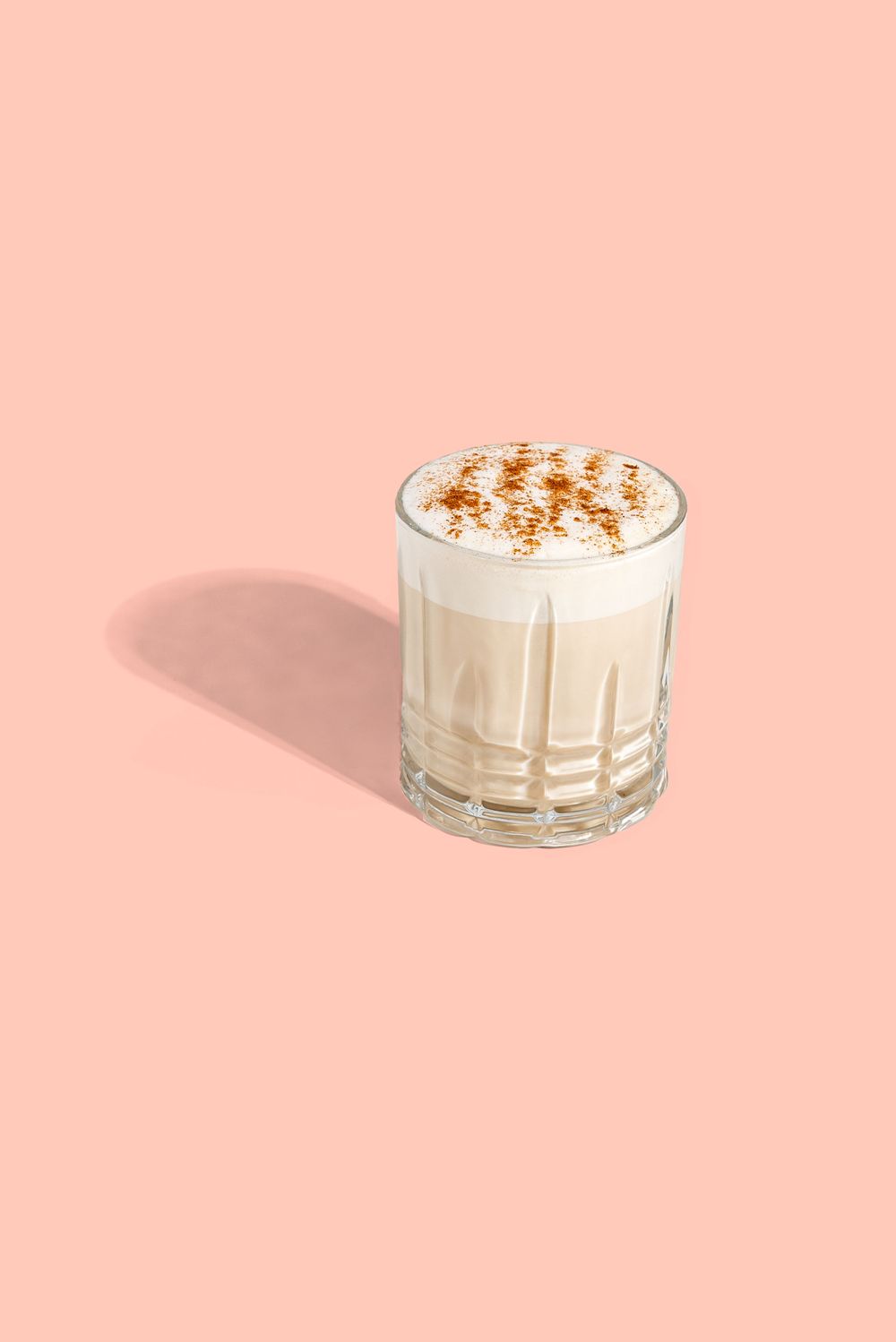 Creamy beverage topped with spices in a clear glass against pink background. Mtlshutter photography