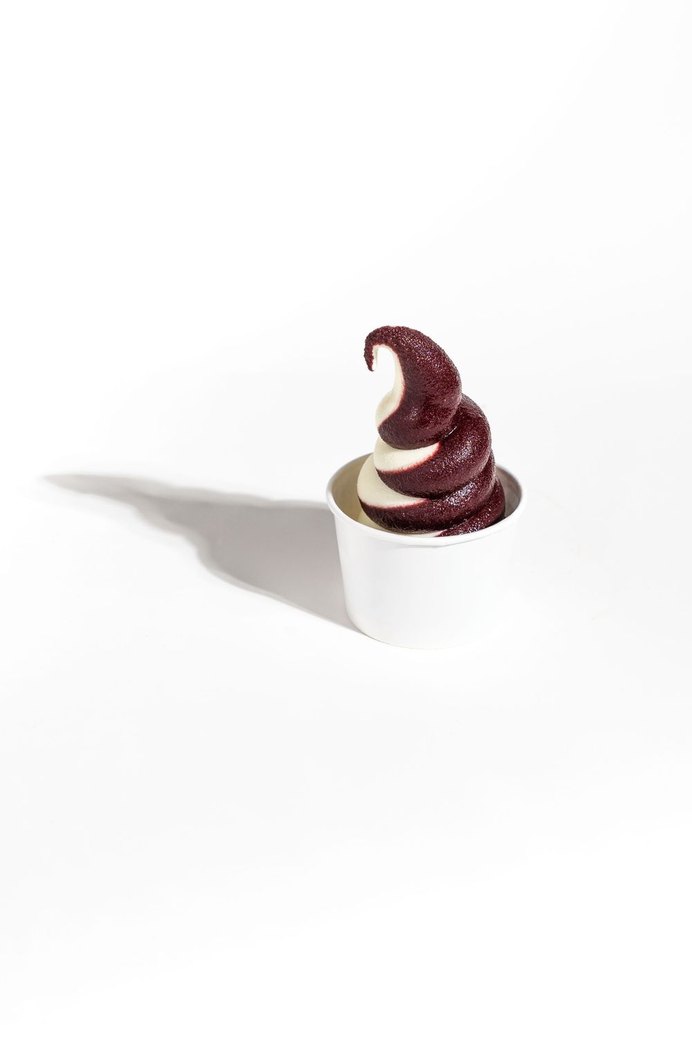 A soft serve ice cream swirl in chocolate and vanilla flavors served in a white paper cup against a plain background. Mtlshutter photography