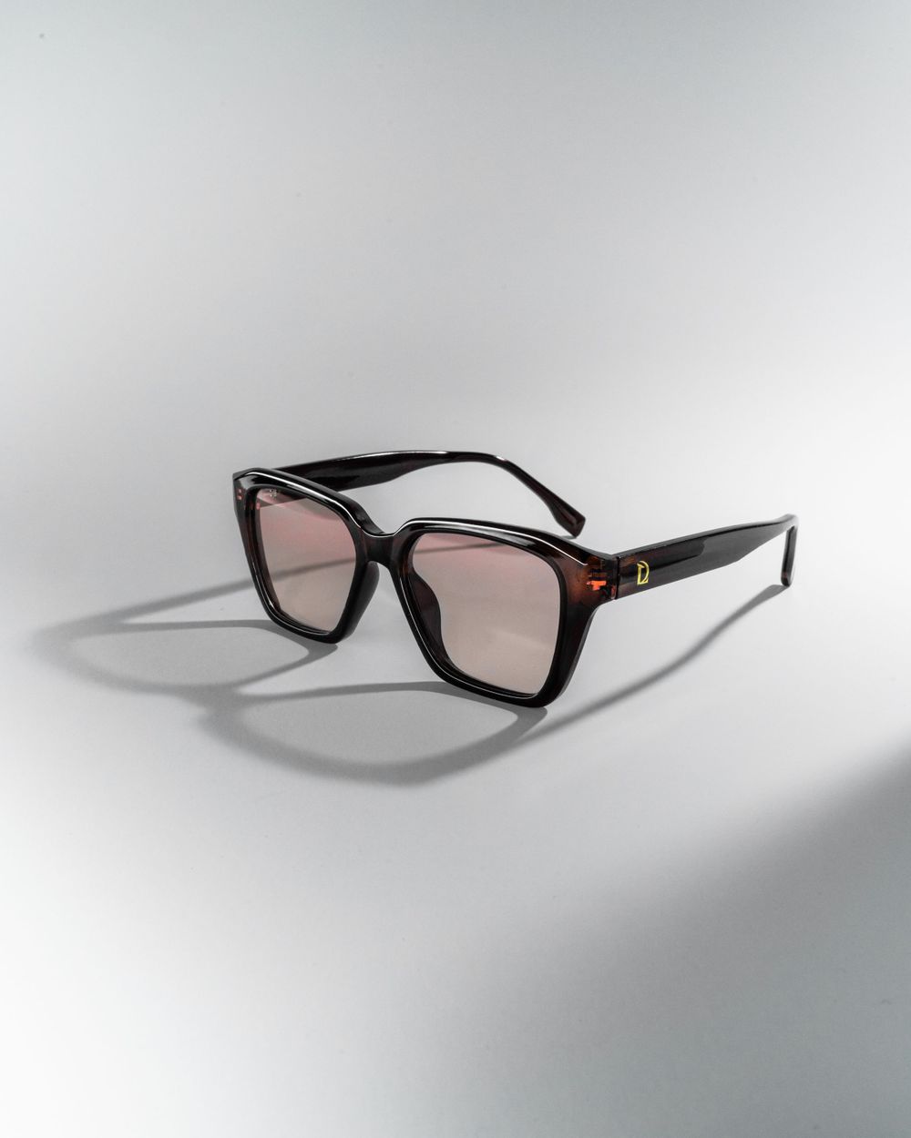 Stylish black square sunglasses with light tinted lenses and gold accent details on a white background. Mtlshutter photography