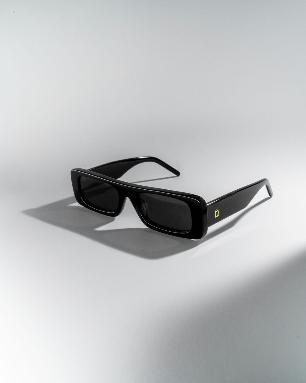 Black rectangular sunglasses with dark lenses displayed on white surface casting shadow. Mtlshutter photography
