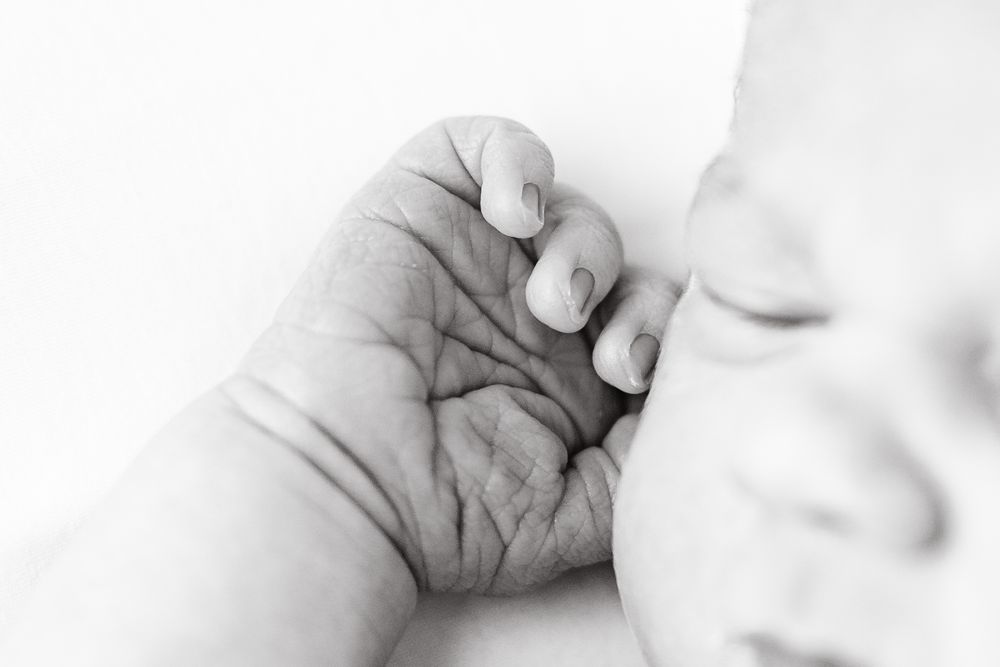 A close-up black and white image of a baby's tiny hand grasping an adult's finger.