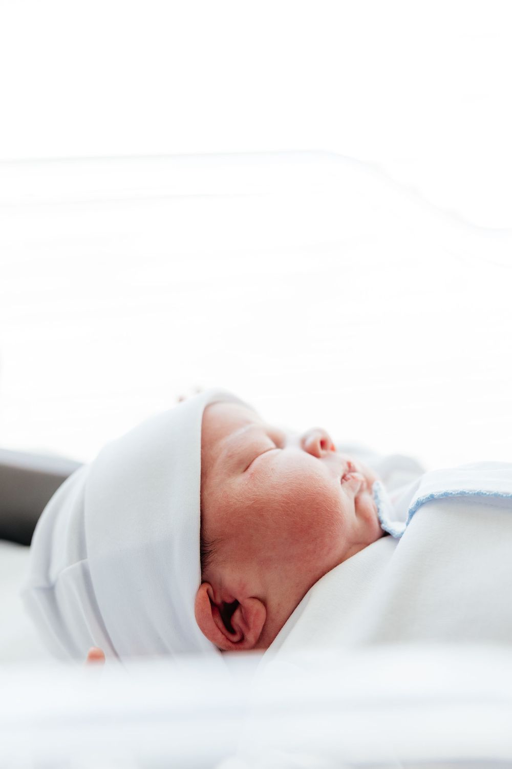A sleeping newborn baby swaddled in white blankets lies peacefully on a white surface.