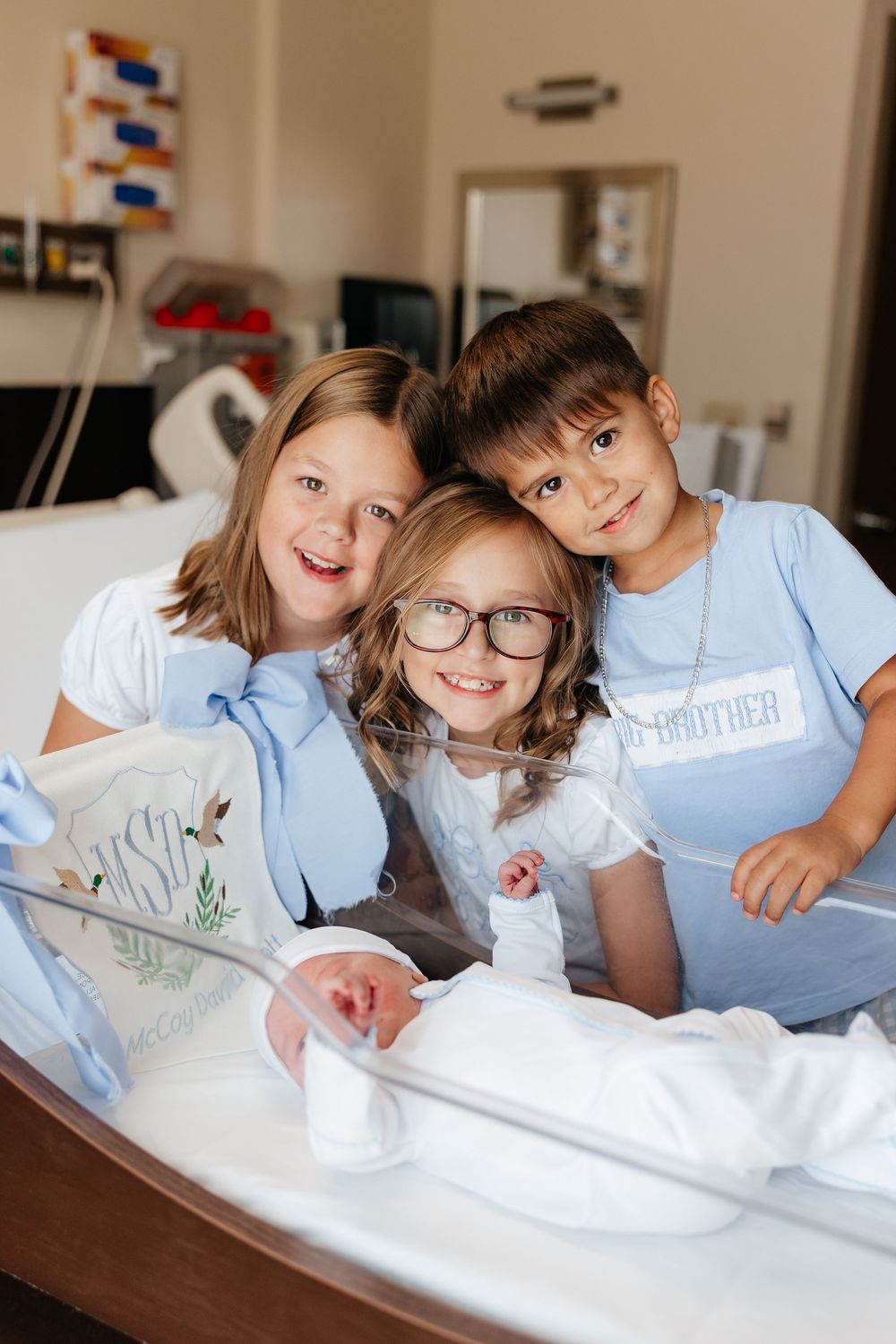 Three children sitting together on a hospital bed sharing a sweet moment.