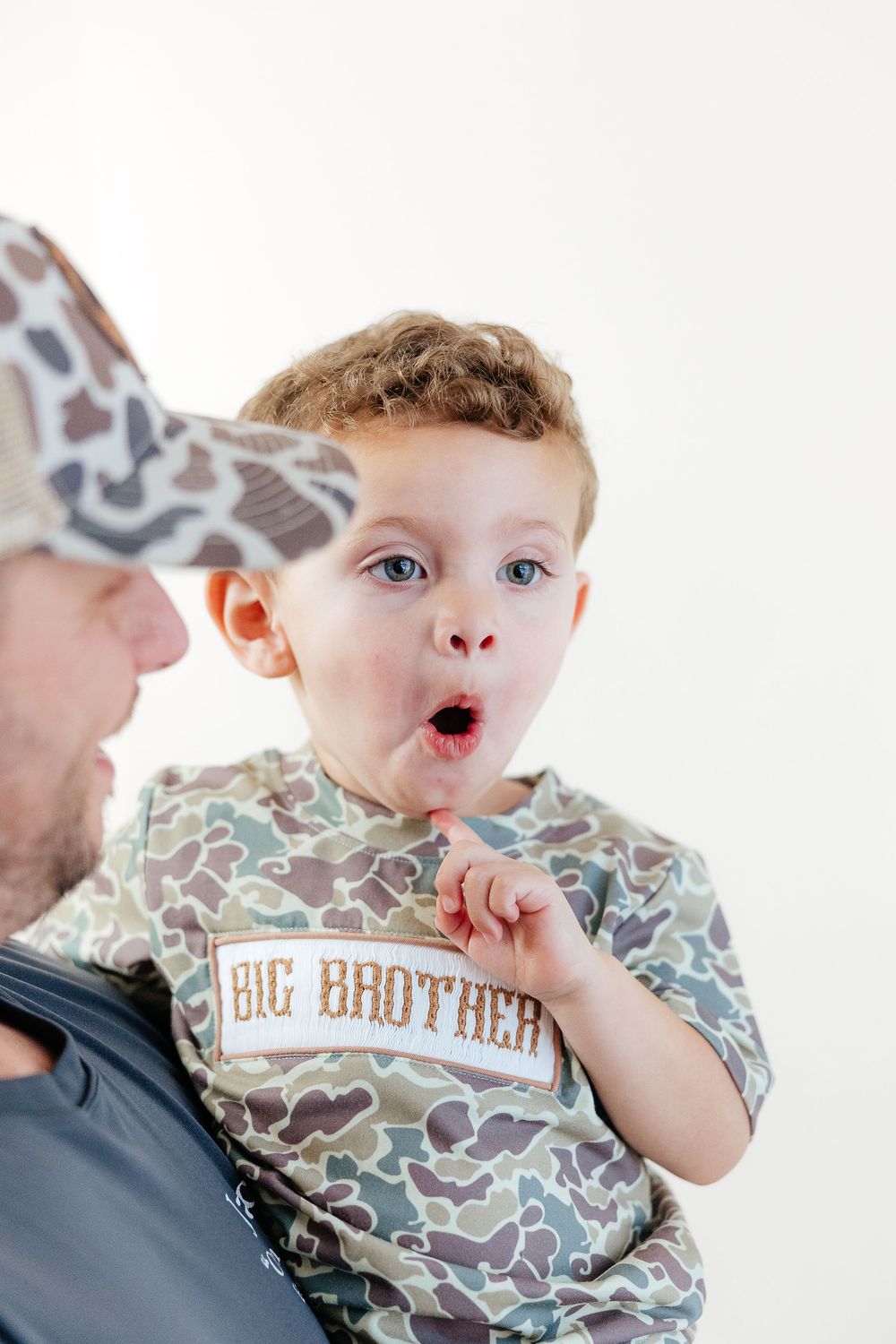 A baby wearing a camouflage pattern 'Big Brother' shirt makes expressive faces in a series of photos.