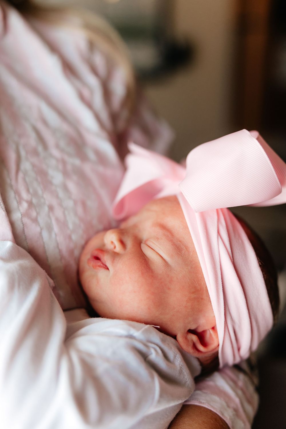 A sleeping newborn baby swaddled in soft pink blankets rests peacefully against white bedding.