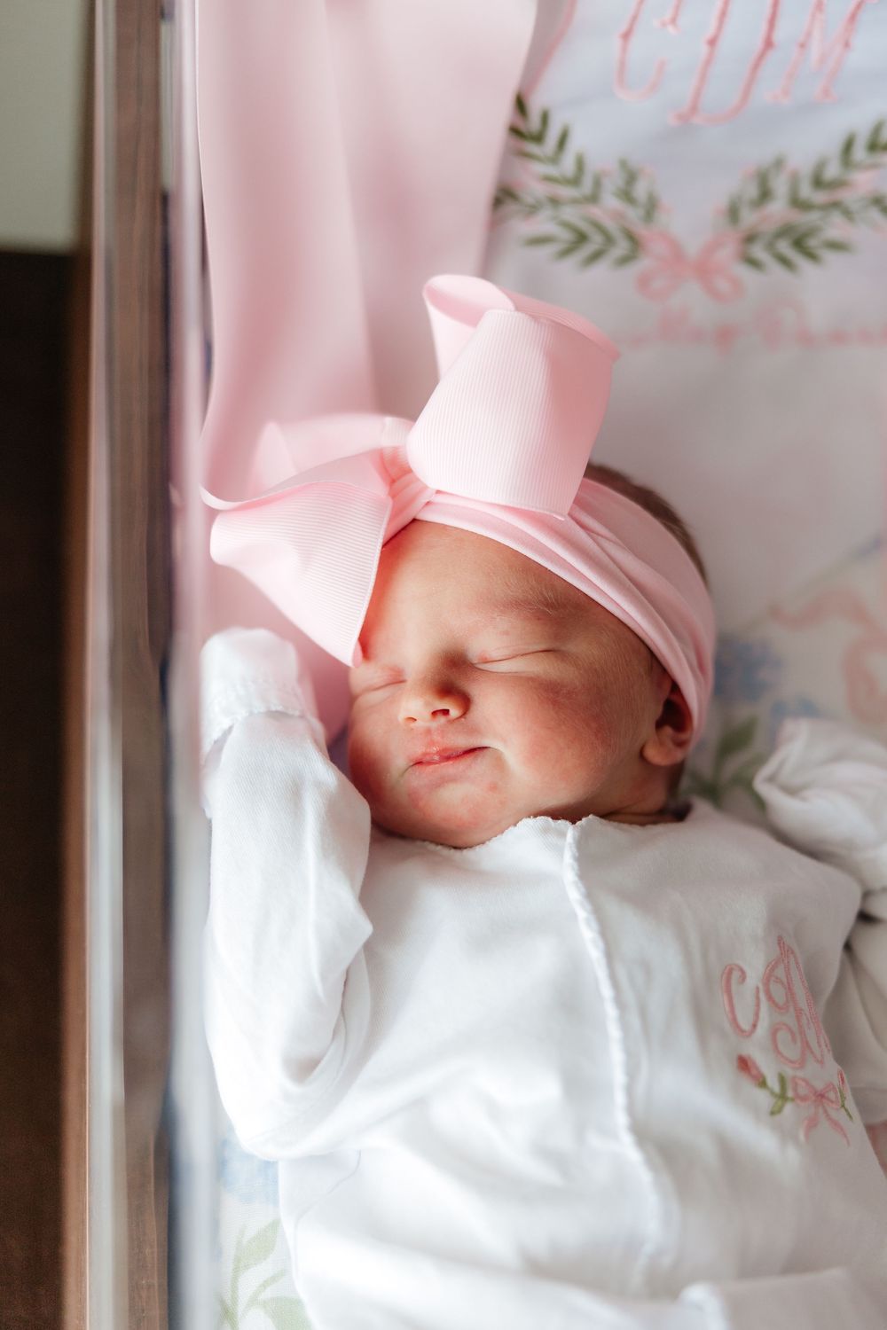 A sleeping baby in pink and white clothing rests peacefully against a floral patterned background.