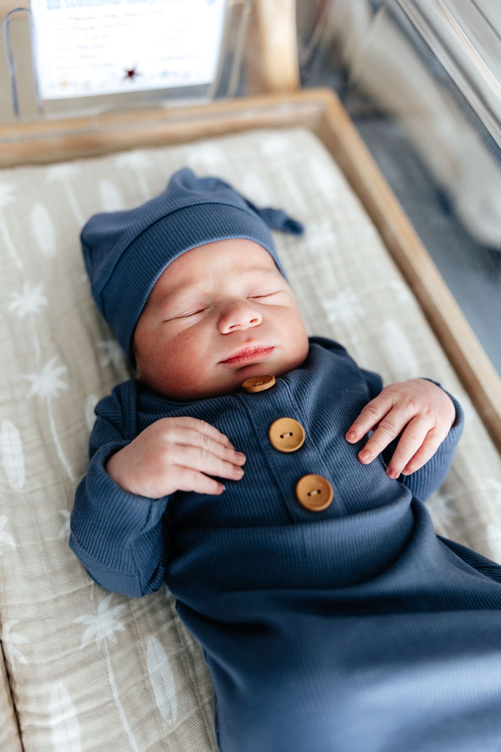 Sleeping newborn baby wearing navy blue outfit with wooden buttons rests peacefully in winter setting.