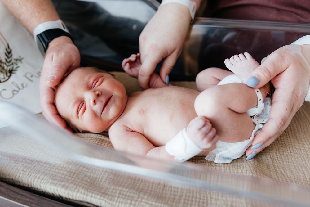 Newborn baby smiling while being held by two adults during a hospital checkup after birth.