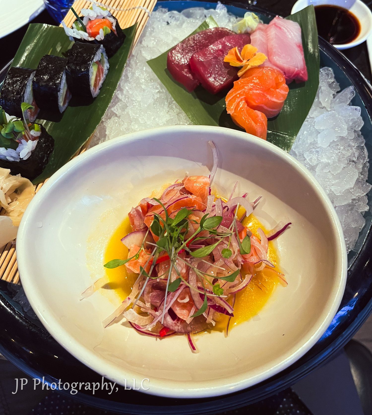 Elegant sashimi and sushi platter with colorful garnishes served on bamboo mat with dipping sauce.