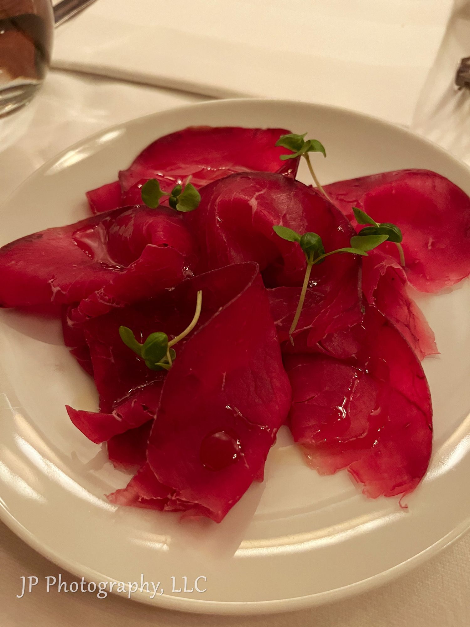 Thinly sliced red tuna sashimi artfully plated with microgreens on white dishes.