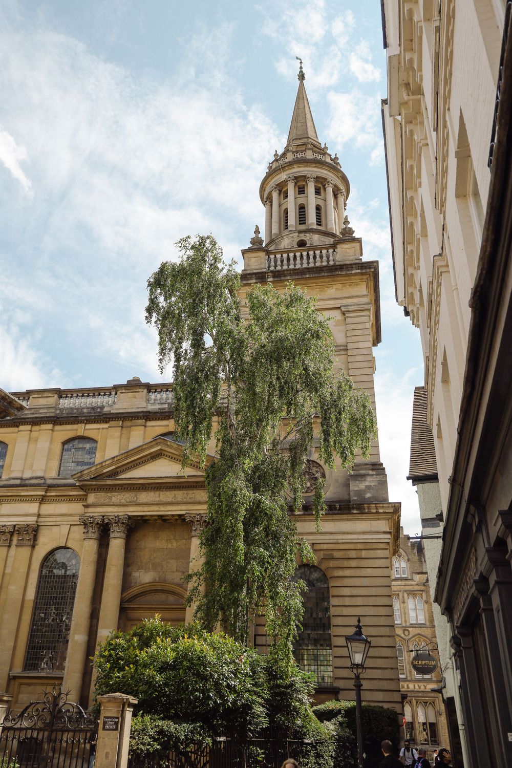 Historic stone church with ornate bell tower and spire framed by a weeping tree in Oxford.