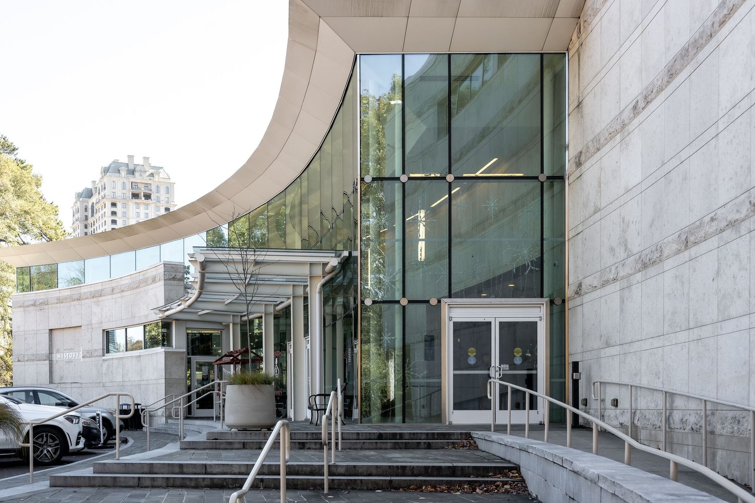 Modern curved concrete building entrance with glass doors and wheelchair accessibility ramp.